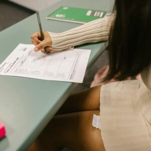 Student secretly looking at a cheat sheet under the desk while taking an exam in a classroom setting.